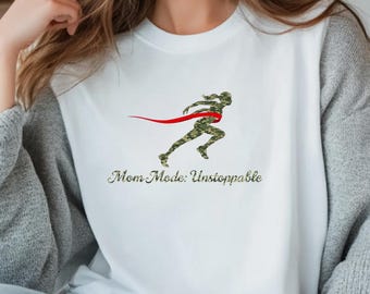 May include: White sweatshirt with a running figure in camouflage print and a red ribbon. The text "Mom Mode: Unstoppable" is printed below the figure in a green font. The sweatshirt has long sleeves.
