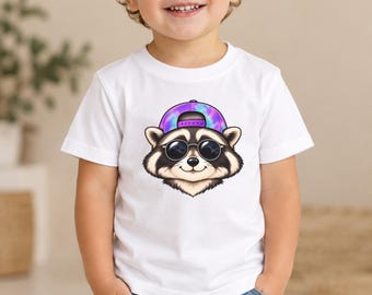 May include: A white short-sleeved t-shirt featuring a graphic print of a raccoon wearing round black sunglasses and a purple and blue tie-dye baseball cap. The raccoon has a light brown and white face with dark fur around the eyes and ears.