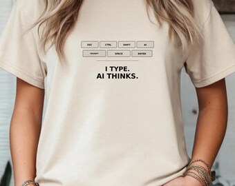 May include: A beige t-shirt with a keyboard layout graphic and the text "I TYPE. AI THINKS." The design includes labels like ESC, CTRL, SHIFT, AI, PROMPT, SPACE, and ENTER, suggesting a tech or computer-related theme.