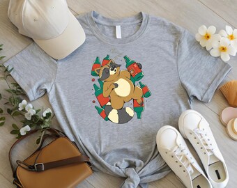 May include: A light gray t-shirt featuring a cartoon raccoon surrounded by beer bottles. The raccoon is brown, tan, and black, with a white belly and a striped tail. The bottles are green and red. A beige baseball cap and white sneakers are also visible.