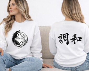 May include: White sweatshirt featuring a black and white yin-yang design with the word "BALANCE" and Japanese characters. The back of the sweatshirt displays Japanese characters. The sweatshirt is worn by a person.