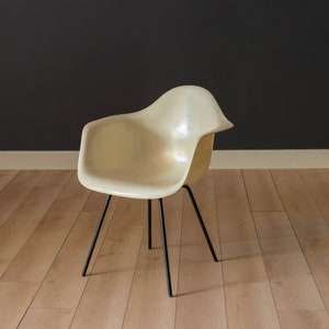May include: A white fiberglass chair with black metal legs. The chair is sitting on a wooden floor.