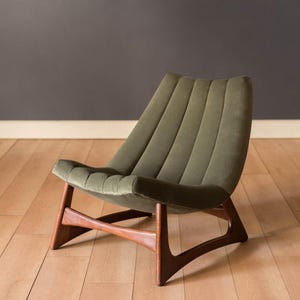 May include: An olive green, mid-century modern chair with a curved back and wooden frame. The chair has a low profile and is upholstered in a soft, ribbed fabric. The wooden legs are a dark brown color.