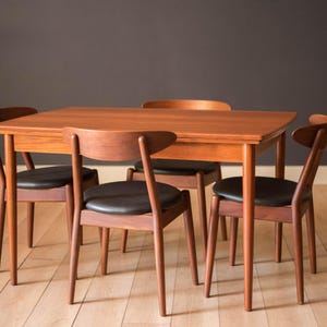 May include: A mid-century modern dining set featuring a rectangular wooden table and four matching chairs. The chairs have black leather seats and curved wooden backs. The table and chairs are made of a warm-toned wood.