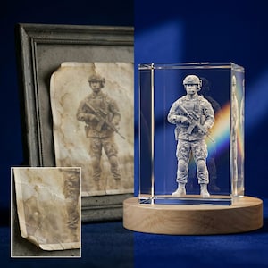 May include: A clear, rectangular crystal sculpture of a soldier in camouflage uniform, mounted on a round wooden base. The sculpture is a detailed 3D rendering. An aged photograph of the same soldier is in a dark frame to the left.
