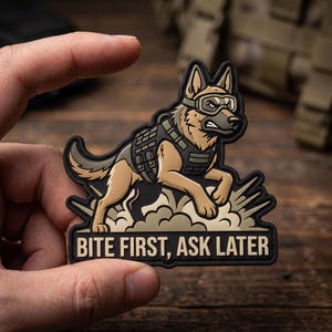 May include: A tactical morale patch featuring a tan and black German Shepherd dog wearing tactical goggles and a vest. The dog is depicted in a dynamic pose amidst a cloud of dust. The text BITE FIRST, ASK LATER is printed in bold letters.