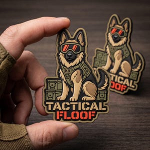 May include: A rubberized morale patch featuring a cartoon German Shepherd dog wearing tactical K9 gear and orange-tinted goggles. The dog sits beside green storage crates. The text TACTICAL FLOOF is printed in bold tan and orange lettering.