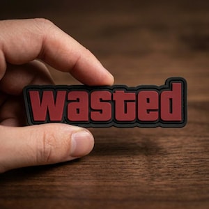 May include: A rectangular patch with a black border and a matte finish featuring the word "wasted" in bold, dark red, sans-serif capital letters. The design has a raised, three-dimensional appearance with clean edges and a uniform, solid color scheme.