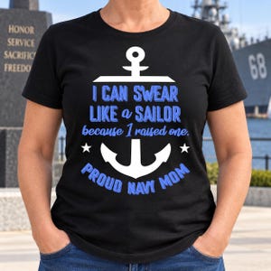 May include: A black short-sleeved t-shirt featuring a white anchor graphic and blue text that reads: I CAN SWEAR LIKE a SAILOR because I raised one. PROUD NAVY MOM. The design includes two small white stars flanking the anchor base.