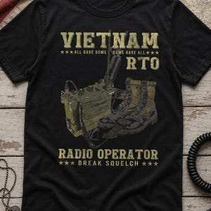 May include: A black t-shirt featuring a graphic print of a military radio, a rifle, and combat boots. The text reads VIETNAM, ALL GAVE SOME SOME GAVE ALL, RTO, RADIO OPERATOR, and BREAK SQUELCH in a distressed, tan-colored, block-style font.