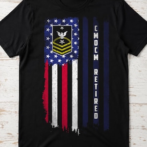 May include: A black short-sleeve t-shirt featuring a distressed American flag graphic. The design includes a Command Master Chief Petty Officer insignia with an eagle and stars, and the vertical white text CMCM RETIRED on the right side.
