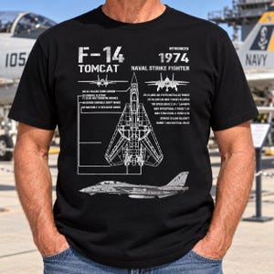 Könnte beinhalten: Ein schwarzes Kurzarm-T-Shirt mit einem weißen Grafikdruck eines F-14 Tomcat Kampfflugzeugs. Das Design zeigt technische Zeichnungen, den Text F-14 TOMCAT, INTRODUCED 1974 sowie detaillierte technische Spezifikationen in imperialen Einheiten.