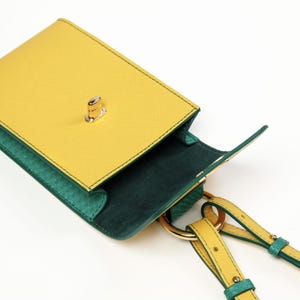 Puede incluir: Un bolso peque&ntilde;o rectangular con un exterior amarillo brillante de acabado texturizado y un cierre giratorio de metal dorado. El interior est&aacute; forrado en verde oscuro y el bolso incluye una correa amarilla y verde unida con anillas doradas.