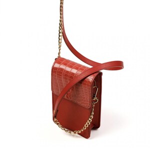 Puede incluir: Un bolso bandolera rectangular vertical de color rojo intenso. El bolso presenta una solapa con un patr&oacute;n texturizado de cocodrilo, un cuerpo liso mate, un detalle de cadena de metal dorado en la parte delantera y una correa de hombro roja a juego.