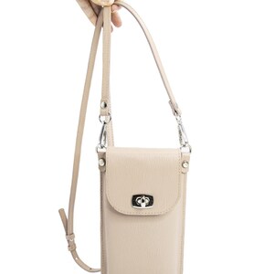 Puede incluir: Un bolso bandolera vertical para tel&eacute;fono de color beige con superficie texturizada, que presenta un cierre giratorio de metal plateado en la solapa frontal y una correa ajustable a juego sujeta con clips giratorios de metal plateado.
