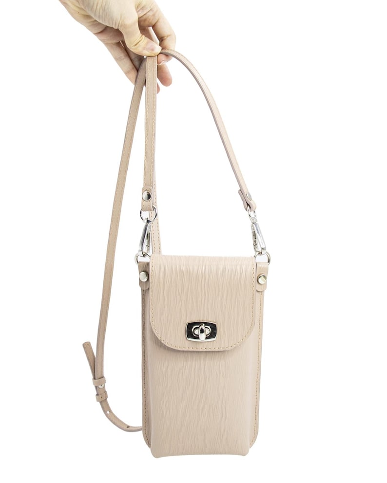 Puede incluir: Un bolso bandolera vertical para tel&eacute;fono de color beige con superficie texturizada, que presenta un cierre giratorio de metal plateado en la solapa frontal y una correa ajustable a juego sujeta con clips giratorios de metal plateado.