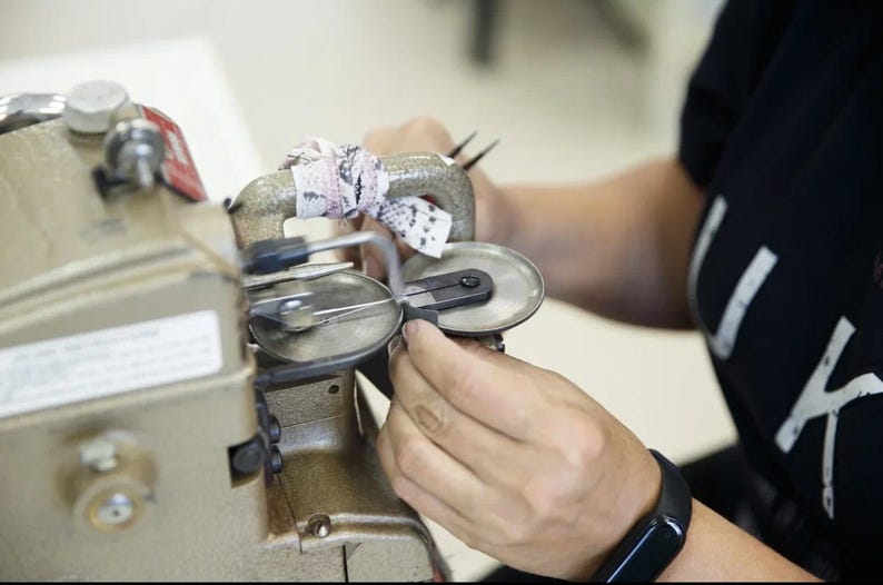 Puede incluir: Una m&aacute;quina de coser industrial de color beige con un asa met&aacute;lica envuelta en una tira de tela estampada. La m&aacute;quina cuenta con dos placas met&aacute;licas circulares y un mecanismo de aguja para coser, con un dial de control negro en el lateral.