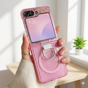 May include: A pink glitter phone case with a ring holder. The case is open, revealing the phone screen displaying the time 7:20 AM. The case has a camera cutout and a white strap for the ring holder.