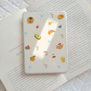 Könnte beinhalten: Weißes Handycase mit Frühstücksmotiv. Mit Illustrationen von Pfannkuchen, Eiern, Croissants, Obst und Kaffee. Enthält hellblaue Schleifenakzente und eine minimalistische Ästhetik.