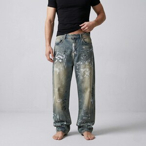 May include: Blue denim jeans with a relaxed fit, featuring white graffiti-style designs. The jeans have a faded wash and a classic five-pocket design. The model is wearing a black t-shirt.
