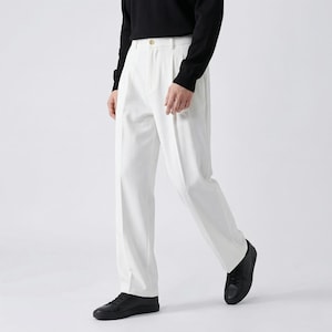 Pu&ograve; includere: Pantaloni bianchi a pieghe con chiusura a bottone, abbinati a una maglia nera a maniche lunghe e scarpe da ginnastica nere. I pantaloni hanno una vestibilit&agrave; ampia. L'outfit &egrave; adatto a occasioni casual o semi-formali.