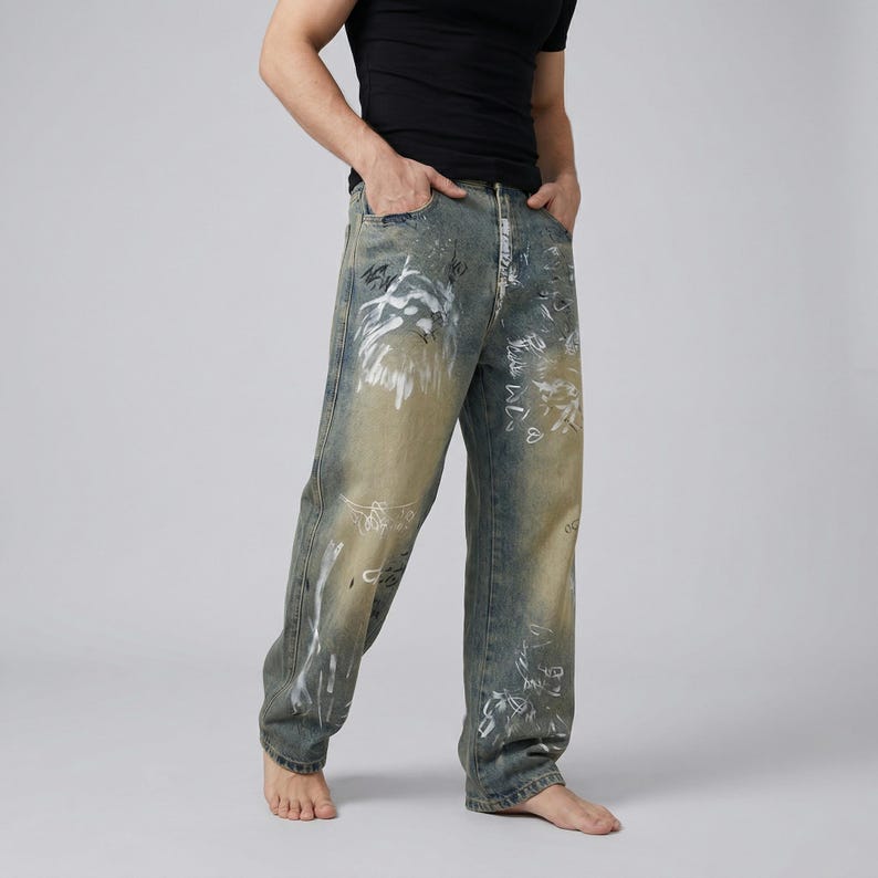 May include: Faded blue denim jeans with white paint-like designs. The jeans have a relaxed fit and a light wash, with distressed details. The overall style is casual and artistic.
