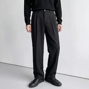 Pu&ograve; includere: Pantaloni neri a pieghe con gamba dritta, abbinati a un top nero a maniche lunghe e scarpe nere. I pantaloni hanno un design classico con chiusura a bottone e zip. L'outfit &egrave; monocromatico.