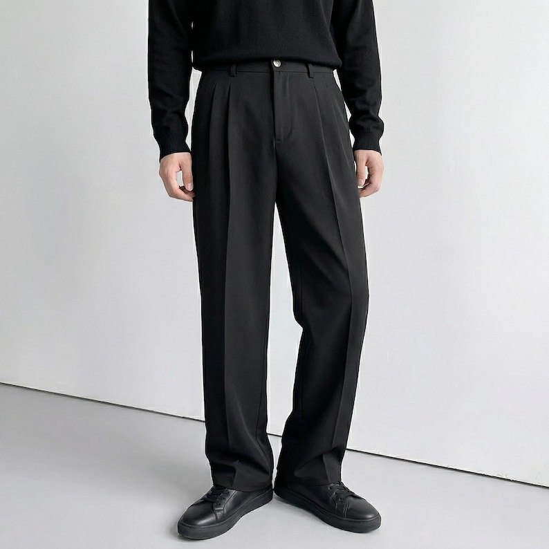 Pu&ograve; includere: Pantaloni neri a pieghe con gamba dritta, abbinati a un top nero a maniche lunghe e scarpe nere. I pantaloni hanno un design classico con chiusura a bottone e zip. L'outfit &egrave; monocromatico.