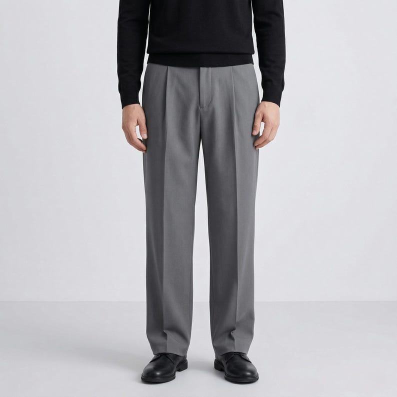 Pu&ograve; includere: Una persona indossa un maglione nero a maniche lunghe e pantaloni grigi a pieghe. I pantaloni hanno un design a gamba dritta e sono abbinati a scarpe in pelle nera. L'outfit &egrave; uno stile classico e minimalista.