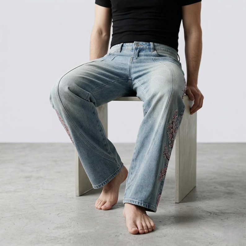 Op de afbeelding: Lichtblauwe denim jeans met decoratieve bloemenborduursels langs de zijnaden. De jeans hebben een relaxte pasvorm en een klassiek vijf-zakken ontwerp. Het model draagt een zwart t-shirt.