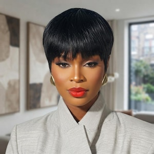 May include: A short, straight black pixie cut wig with bangs, styled with a smooth finish. The hair is dark and uniform in color, framing the face closely. The wig features a layered, textured look that sits neatly around the head and ears.