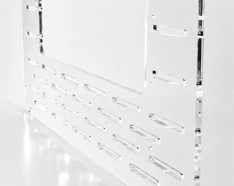 Könnte beinhalten: Eine transparente Acrylplatte mit einem U-förmigen Ausschnitt an der Oberseite und mehreren horizontalen Schlitzen, die in einem Rastermuster über die Oberfläche verteilt sind. Die Platte hat eine glatte, klare Oberfläche mit präzisen Kanten.