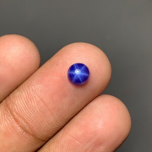 Könnte beinhalten: Ein kleiner, runder, im Cabochon-Schliff gefertigter blauer Sternsaphir-Edelstein mit einem ausgeprägten sechsstrahligen Sternmuster, das mittig auf der Oberfläche erscheint. Der tiefblaue Edelstein hat eine glatte, polierte Oberfläche und glänzt.