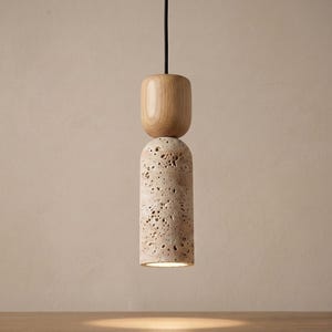 Puede incluir: Una l&aacute;mpara colgante moderna con una base cil&iacute;ndrica de piedra porosa y una parte superior de madera redondeada. La l&aacute;mpara cuelga de un cable negro, mostrando un dise&ntilde;o minimalista. La l&aacute;mpara emite un brillo c&aacute;lido, ideal para la iluminaci&oacute;n interior.