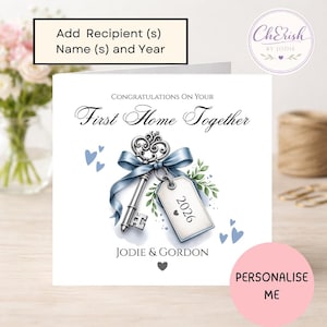 May include: A square greeting card featuring the text Congratulations On Your First Home Together, Jodie & Gordon, and 2026. The design includes an illustration of a silver skeleton key tied with a blue ribbon and a tag, surrounded by small blue hearts.
