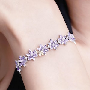 May include: A silver bracelet featuring a floral design with purple petals and small, clear gemstones. The bracelet is composed of multiple flower-shaped links, creating a delicate and elegant accessory.