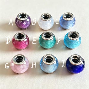 Puede incluir: Nueve cuentas de abalorios de colores con detalles metálicos plateados. Las cuentas son de varios colores, incluyendo morado, blanco, azul, rosa y verde azulado. Cada cuenta tiene un diseño facetado o estampado único. Letras de la A a la I.