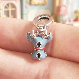 K&ouml;nnte beinhalten: Ein silberner Charm mit einem blau-roten Emaille-Stitch-Design. Der Charm hat oben eine kleine Schlaufe mit dem Disney-Logo. Die Stitch-Figur hat einen roten Kragen und hebt die Arme.
