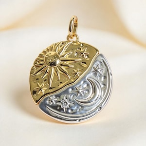 May include: A circular pendant featuring a two-tone design with a gold-coloured sun and stars on one half and a silver-coloured crescent moon and stars on the other. The pendant includes a small circular bail at the top for attachment to a chain.
