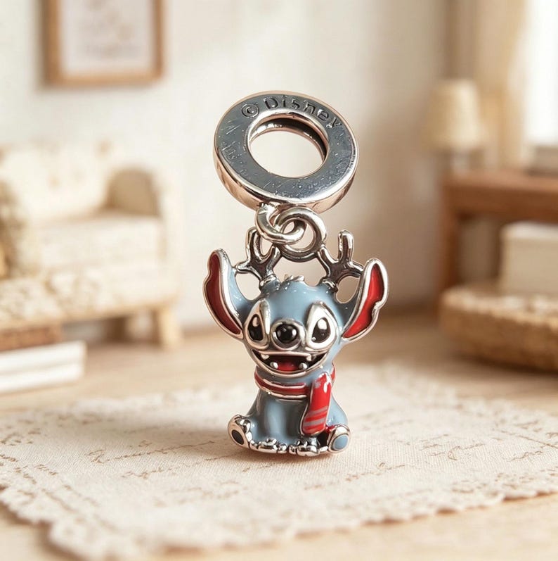 K&ouml;nnte beinhalten: Ein silberner Charm-Anh&auml;nger mit der Figur Stitch aus Disneys Lilo & Stitch. Der Anh&auml;nger hat einen blauen K&ouml;rper, rote Ohren und einen roten Schal. Der Anh&auml;nger ist an einem silbernen Ring mit dem eingravierten Wort "Disney" befestigt.