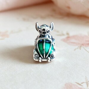 May include: A silver charm featuring a cartoon character in a green and silver car. The charm has a detailed design with a green center and is likely made of sterling silver.