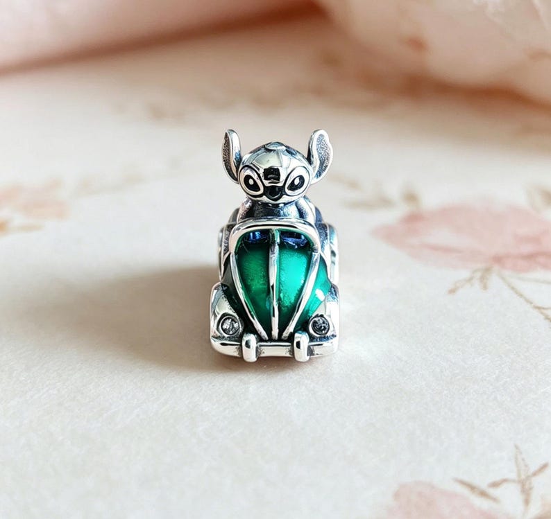 May include: A silver charm featuring a cartoon character in a green and silver car. The charm has a detailed design with a green center and is likely made of sterling silver.