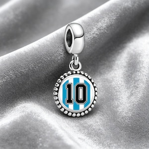 Pode incluir: Um berloque de prata com um pingente redondo com o número 10 em preto sobre um fundo listrado azul e branco. O berloque tem uma borda com contas e uma argola para prender a uma pulseira ou colar.