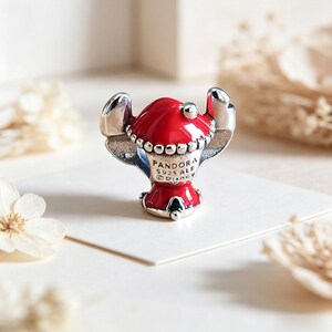 Op de afbeelding: Een Pandora-bedel met een rood en zilver karakterontwerp. De bedel heeft een rode kop en lichaam met zilveren details, inclusief de oren. De bedel is gemarkeerd met "Pandora S925 ALE Disney".