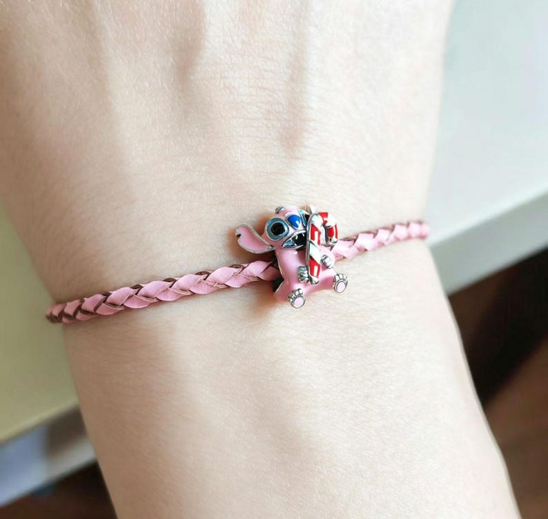 Pu&ograve; includere: Bracciale in pelle intrecciata rosa chiaro con un charm di Stitch rosa con occhi blu e un bastoncino di zucchero. Il charm presenta dettagli rossi, bianchi e argentati. Il bracciale &egrave; di colore rosa chiaro.