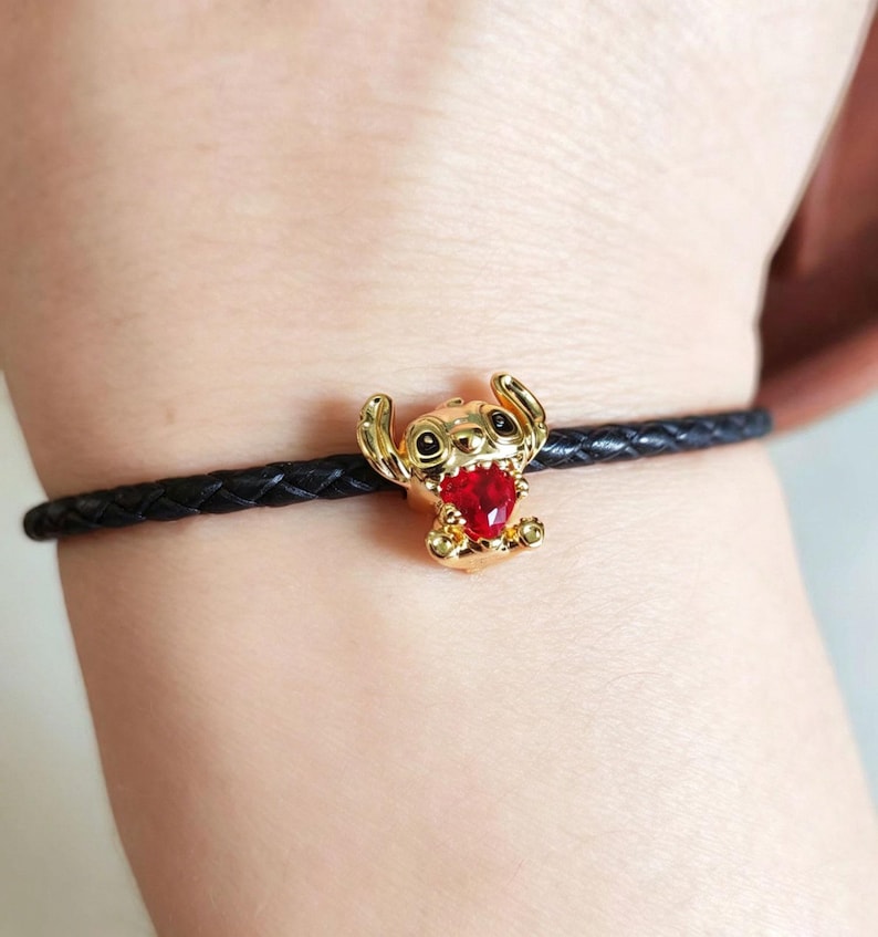 Peut inclure: Bracelet avec un charm dor&eacute; repr&eacute;sentant Stitch, orn&eacute; d'un c&oelig;ur rouge. Le charm est fix&eacute; &agrave; un bracelet en cuir tress&eacute; noir. Accessoire sur le th&egrave;me de Disney.