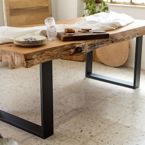 May include: A rustic wooden dining table with a live edge and black metal legs. The table is set with plates, glasses, and a wooden cutting board. A white cloth is draped across the table. The table is approximately 72 inches long.
