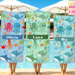 May include: Three personalized beach towels with aquatic-themed designs. Each towel features a different color scheme: blue, green, and teal. The towels are decorated with cartoon sea creatures, including octopuses, jellyfish, dolphins, and sharks. Each towel has a name on it.