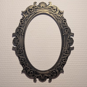 Könnte beinhalten: Verzierter ovaler Bilderrahmen mit dunkler Bronzeoberfläche. Der Rahmen weist aufwendige Schnörkel und muschelförmige Akzente auf. Die leere Mitte ist bereit für ein Foto oder Kunstwerk. Ein dekoratives Element.