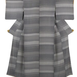 Puede incluir: Un kimono gris con rayas horizontales en diferentes tonos de gris. Las mangas son rectangulares y la prenda tiene una falda ancha. Se ven detalles dorados en las aberturas de las mangas. El kimono se muestra sobre un fondo blanco.